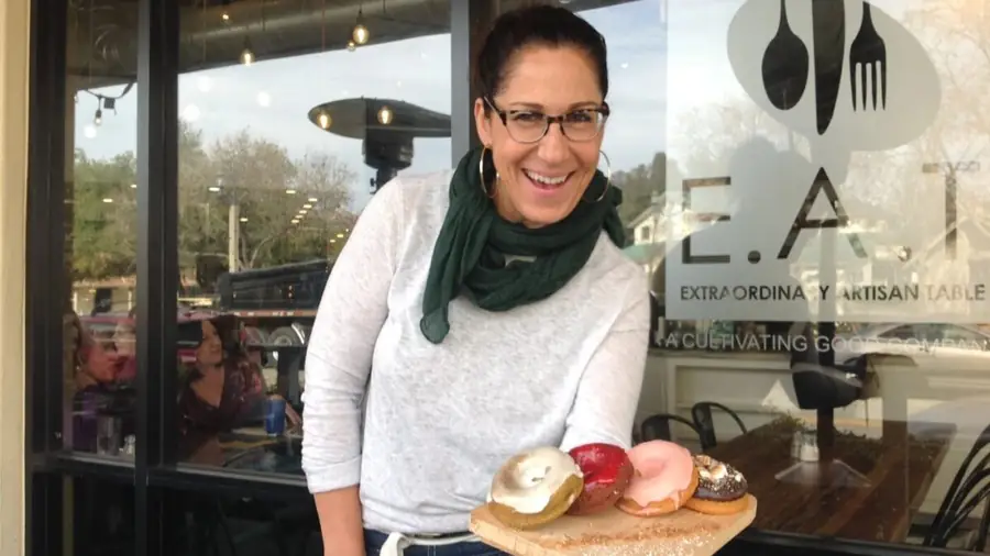 E.A.T. Marketplace founder holding a tray of colorful baked goods outside the café